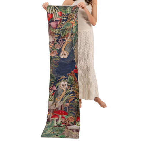 Person holding a long, colorful scarf with nature-themed design featuring owls and mushrooms.