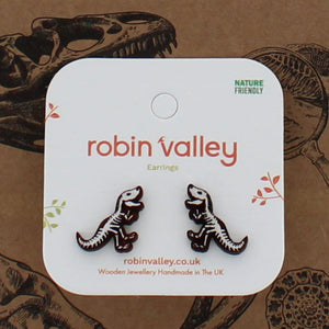 Earrings with dinosaur skeleton design on a 'Robin Valley' branded card against a brown background with illustrations.