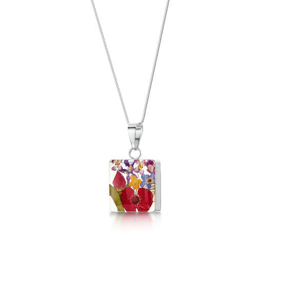 Necklace with a silver chain and a pendant of a square block of resin encasing a mixed set of flowers.